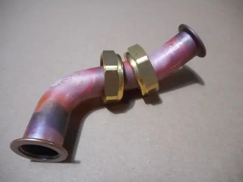 Remeha-Rohr mit einer gebogenen Form, ausgestattet mit zwei goldenem Verschlüssen. Das Material scheint Kupfer zu sein, erkennbar an der Oberflächenfärbung.